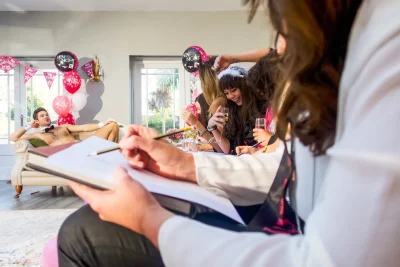Hens laughing and sketching a posing butler during a life drawing class at a hen party